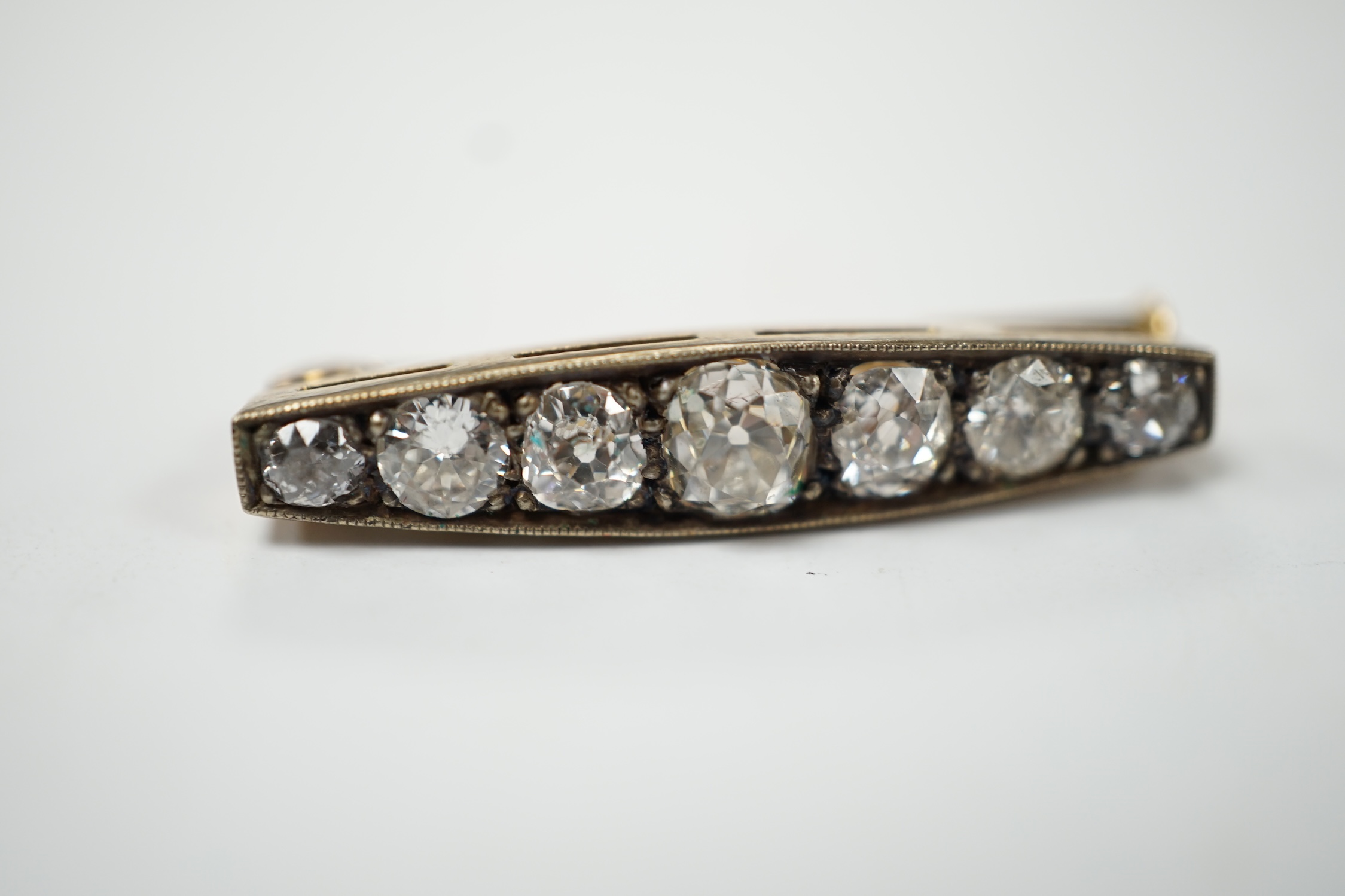 A small yellow metal and seven stone graduated diamond set bar brooch, 28mm, gross weight 3.9 grams (two cracks to one stone). Fair condition.